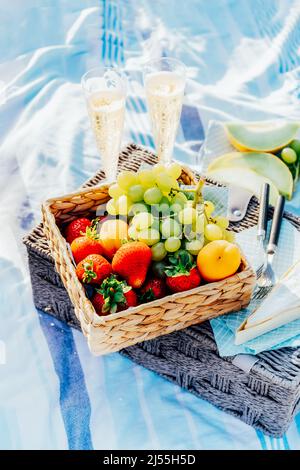 Sommerpicknick am Strand bei Sonnenuntergang. Picknick-Essen: Obst, Käse und Gläser Champagner oder Wein für zwei Personen auf einem Korbkorb auf der Decke. Romantisches Date Stockfoto