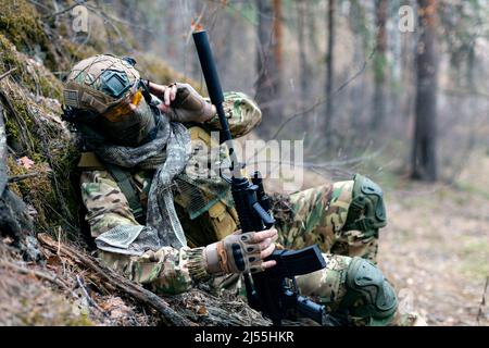 Foto eines Soldaten der Spezialeinheiten während eines Zusammenstoßes im Wald. Er ruft die Unterstützung seiner Gruppe beim Walkie-Talkie an. Das Konzept der modernen militäroper Stockfoto