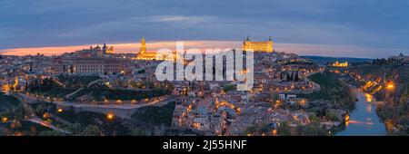 Ein breites Panoramabild von einem Abend in Toledeo mit Blick auf die Kathedrale (Catedral de Santa María de Toledo) und den Alcazar von Toledo. Stockfoto