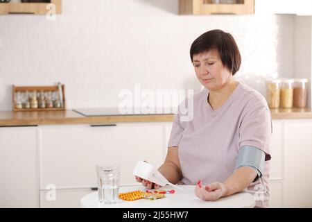 Kranke ältere Frauen kümmern sich um die Gesundheit, verwenden Sphygmomanometer zur Messung von Blutdruck, Puls und Herzfrequenz selbst und nehmen Medikamente zu Hause ein. Stockfoto