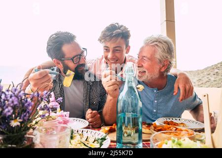 Vater Großvater und Sohn eaing zusammen Spaß haben. Vatertag Konzept Feier mit Männern Familie genießen Mahlzeit auf dem Tisch. Fröhlicher junger Mann Stockfoto