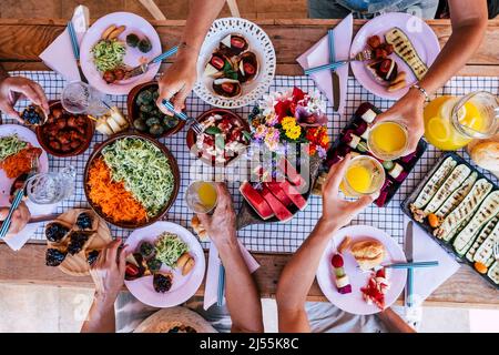 Friendhsip und Familienfeier zur Mittagszeit in der oberen vertikalen Ansicht. Eine Gruppe von Menschen, die zusammen auf dem Tisch essen. Menschen, die Essen aus Speisen und Stockfoto