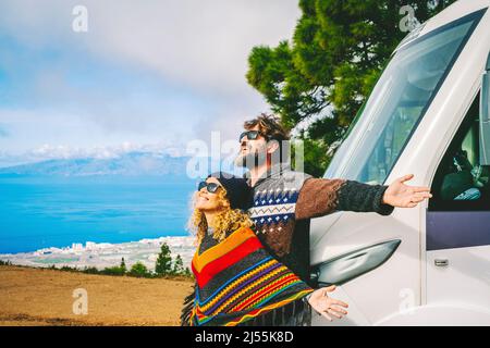 Van Leben und Reiseziel Konzept. Mann und Frau freuen sich über die Neuankunft in der Natur und öffnen die Arme gegen ihren neuen modernen Wohnmobil. Stockfoto