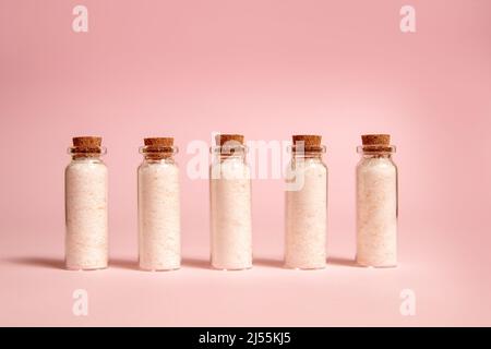 Rosafarbenes Himalaya-Salz in Glasflaschen. Kleine Flaschen mit Korkstopfen. Rosa Hintergrund. Stockfoto