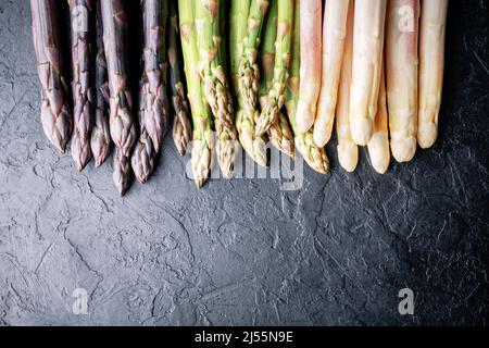 Grüne, violette und weiße Spargelsprossen auf schwarzem Brett Draufsicht flach liegend. Food-Fotografie Stockfoto