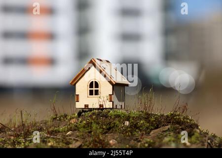 Holzhausmodell auf dem Hintergrund von Hochhäusern. Konzept von Landhaus, Immobilien in ökologisch sauberer Umgebung Stockfoto