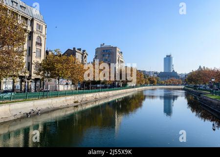 Bukarest, Rumänien, 22. November 2020: Landschaft mit Dambovita-Fluss, alten Gebäuden und gelben, orangen und braunen Blättern in großen Bäumen in der Mitte Stockfoto