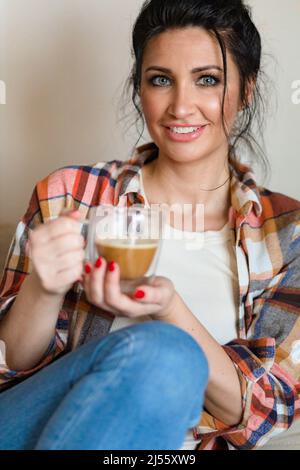 Blauäugige Frau mittleren Alters, die mit einer Tasse Kaffee sitzt Stockfoto