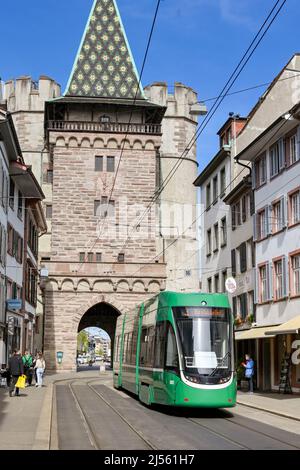 Basel, Schweiz - April 2022: Moderne elektrische Straßenbahn auf einer Straße in der Nähe des Stadtzentrums mit dem Turm des Spalentors im Hintergrund Stockfoto