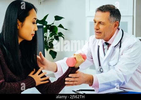 Arzt Physiotherapeut hilft dem Patienten Hantel mit einer Hand in seinem Büro zu heben. Klinik für die Gesundheitsbranche Stockfoto