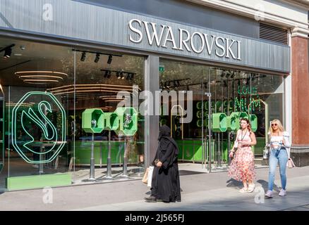 Drei Frauen, die an einer Niederlassung von Swarovski, einem Einzelhändler für Kristallglas, Schmuck und Accessoires, in der Oxford Street, London, Großbritannien, vorbeigehen Stockfoto