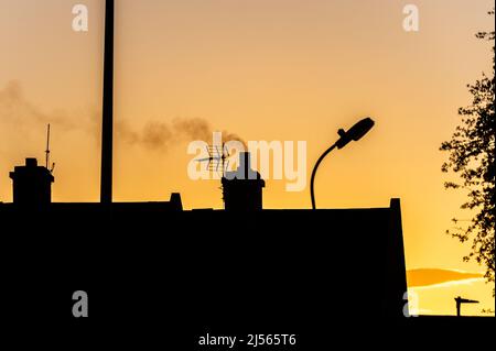Rauch steigt bei Sonnenuntergang aus einem Hauskamin in Irland auf. Stockfoto