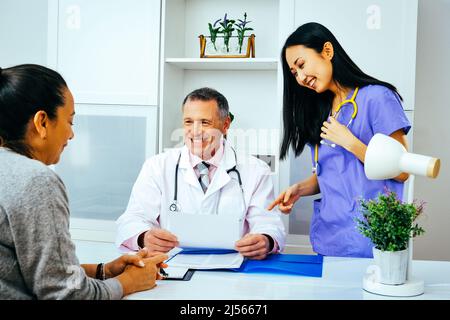 Glücklicher Arzt und Krankenschwester im Gespräch mit erwachsenen weiblichen Patienten in Krankenhausberatung Gesundheitsbranche Stockfoto