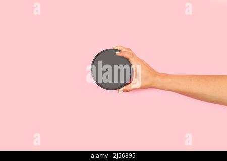 Frau Hand hält einen runden Pappdeckel auf einem rosa Hintergrund mit Kopierraum Stockfoto