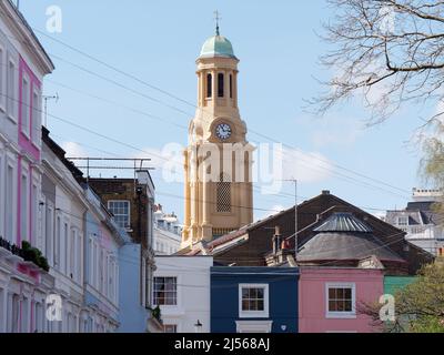 London, Greater London, England, April 09 2022: Farbenfrohe Immobilien an der Portabello Road in Notting Hill mit dem Glockenturm der St. Peters Kirche dahinter Stockfoto