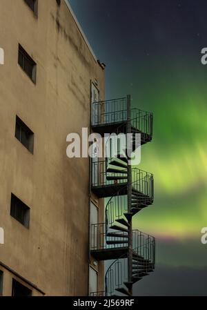 nordlichter aurora Borealis Himmel und Sicherheits-Metalltreppe an der Gebäudeecke mit blauem Himmel im Hintergrund Stockfoto