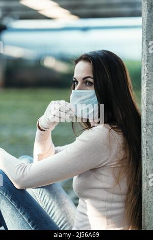 Ein junges Mädchen in Gummihandschuhen sitzt und hält eine schützende Gesichtsmaske Stockfoto