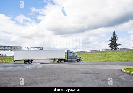 Industrieller leistungsstarker professioneller grauer Langstrecken-Sattelschlepper mit großem Sattelzug, der Ladung im trockenen Kleintransporter transportiert und mit h auf die lokale Straße fährt Stockfoto