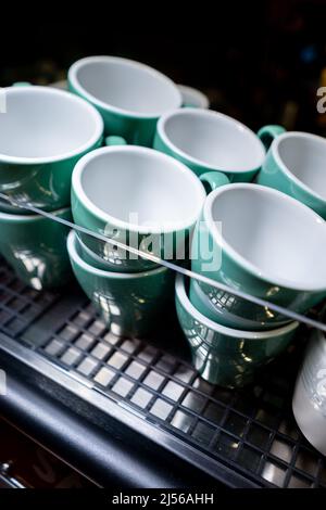Set aus Keramikbechern oder Tassen, die auf einer professionellen Kaffeemaschine erhitzt werden Stockfoto