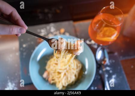 Person isst italienische Carbonara-Pasta mit Meeresfrüchten, Garnelen, aperol-Spritz-Glas Stockfoto