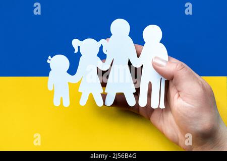 Hand hält weiße Papiersilhouette der ukrainischen Familie. Flach liegend, Draufsicht auf blaugelbem Papierhintergrund, Ukraine-Flaggenfarben. Stockfoto