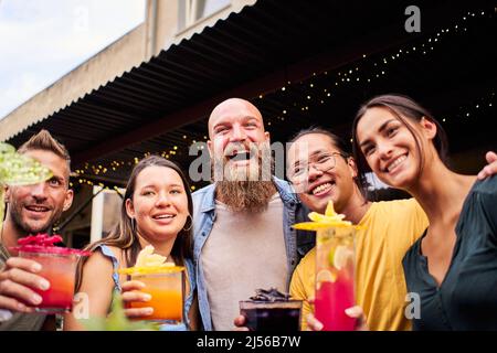 Selfie-Gruppe von Menschen jubelt und hat Spaß. Multirassische glückliche Freunde trinken und toasten Cocktails in der Brauerei-Bar, die zusammen Fotos machen Stockfoto