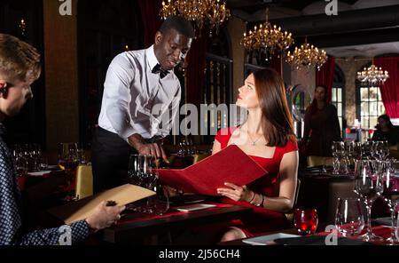 Der Kellner nimmt die Bestellung von einem jungen Paar auf Stockfoto