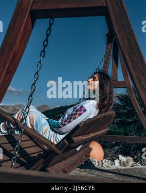 Frau, die Berge auf der Schaukel sitzend beobachtet Stockfoto