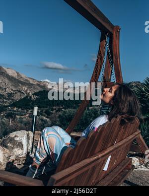 Frau, die Berge auf der Schaukel sitzend beobachtet Stockfoto