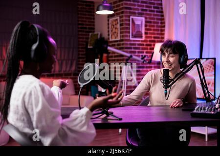 Ein vielfältiges Team von Frauen trifft sich im Studio, um gemeinsam Podcast-Chats zu streamen und Inhalte für den Social-Media-Kanal zu erstellen. Weibliche Influencer, die professionelle Aufnahmesequipment auf der Station verwenden. Stockfoto