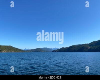 Eintritt zum Jervis Inlet mit den Coast Mountains und gemäßigtem Regenwald an der Sunshine Coast mit blauem Himmel, British Columbia, Kanada Stockfoto