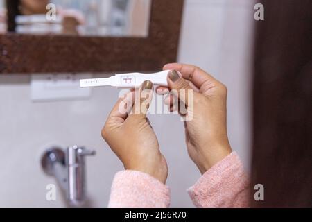 Nahaufnahme der Hände einer nicht erkennbaren Frau mit einem positiven Schwangerschaftstest im Badezimmer ihres Heims Stockfoto