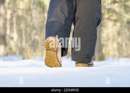Frau, die im Winterwald auf Schnee läuft. Konzentrieren Sie sich auf die Sohle der Show mit Schnee. Stockfoto