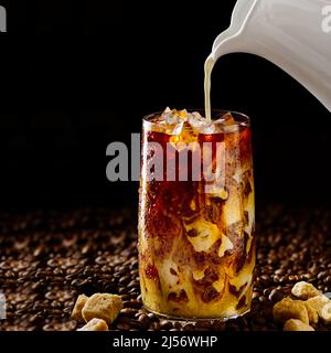 Eiskaffee. Leckerer Eiskaffee mit Milch, kaltes Getränk im Glas mit Eis auf dunklem Kaffeehintergrund. Stockfoto