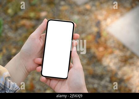 Aufnahme über dem Kopf, weibliche Hände halten ein Smartphone leeren Bildschirm Mockup über verschwommenem Straßenhintergrund Stockfoto