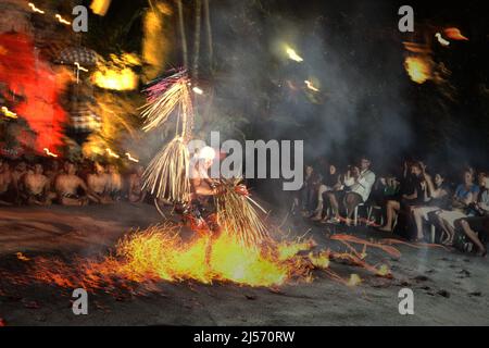 Ein Feuertanzkünstler läuft über einen Haufen brennender Kokosnüsse vor Touristen, während der Kecak- und Feuertanzshow in Ubud, einem wichtigen Touristenziel in Bali, das sich in Gianyar Regency, Bali, Indonesien befindet. Bali war laut TripAdvisor das viertbeliebteste Reiseziel der Welt vor der COVID-Zeit. Das Statistikbüro der Provinz Bali hatte erwähnt, dass 2019 6.275.210 Touristen Bali besuchten – die höchste Rekordzahl. Aufgrund der Pandemie besuchten jedoch nur 1.069.473 Menschen die Insel der Götter im Jahr 2020, gefolgt von nur 51 (100 Prozent Rückgang) im Jahr 2021. Stockfoto