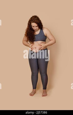 Vertikale verwirrt rothaarige übergewichtige Fett barfuß Frau auf Bauch, tun Aktivität, halten berühren Bauch Stockfoto