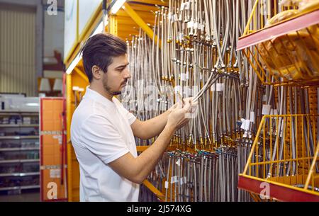 Mann im Geschäft wählt flexible Wasserschläuche mit Metallauslauf für den Anschluss von Sanitäranlagen. Stockfoto