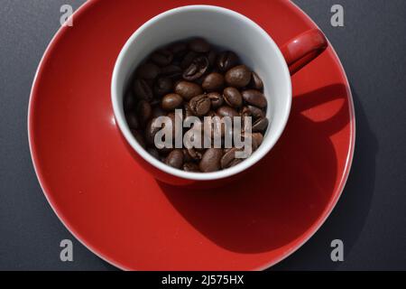 Kaffeebohnen in einer roten Espressotasse von oben auf einem glänzend grauen Hintergrund Stockfoto