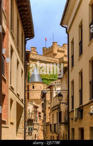 Rustikale mittelalterliche Steinhäuser in einer engen Straße der Altstadt von Olite, Spanien mit Blick auf die prächtige Königspalastburg Stockfoto