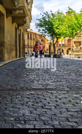 Nahaufnahme einer alten Kopfsteinpflasterstraße mit rustikalen mittelalterlichen Steinhäusern in Olite, Spanien, mit einem unverkennbaren Paar, das in der Ferne zu Fuß unterwegs ist Stockfoto