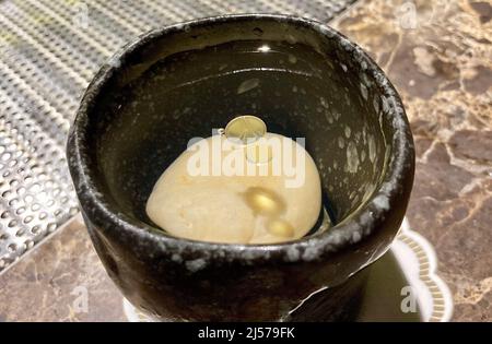 Bangkok, Thailand. 18. April 2022. „Summit“, eine Cocktailkreation aus Steinen, wird in der Bamboo Bar des Mandarin Oriental Hotel serviert. Gin, Pastille, Salbei und Granit sind die Zutaten, mit einem Stein in der Mitte als Eiswürfel. Die Barkeeper kreieren heute innovative Cocktails mit Aromen, die unvergessliche Geschmackserlebnisse bieten - und Zutaten, die man in Getränken nicht erwarten würde. Mixologie ist Kunst und Wissenschaft. (To dpa 'die Essenz der Steine: Wie die Mixologie die Barkultur revolutioniert') Quelle: Carola Frentzen/dpa/Alamy Live News Stockfoto