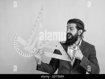 Messen und Größe. Glücklich reifen Lehrer hält Dreieck und Winkelmesser Werkzeug. Bärtiger Mann Ingenieur Arbeit mit Lineal. Bereiten Sie sich auf Geometrie-Prüfung Stockfoto