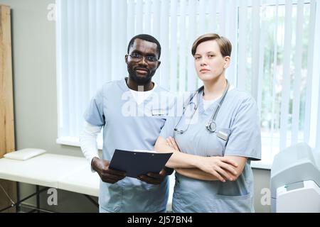 Team von jungen multiethnischen Mitarbeitern der Klinik in Uniform stehen gegen Untersuchungscouch Stockfoto