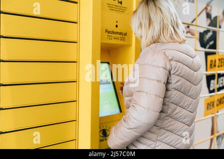 Poznan, Polen - 12. April 2022 Gelbes Shopping-Schließfach inPost mit Frau Eingabe Code, um es zu öffnen. E-Commerce-Versand und Lieferung Stockfoto