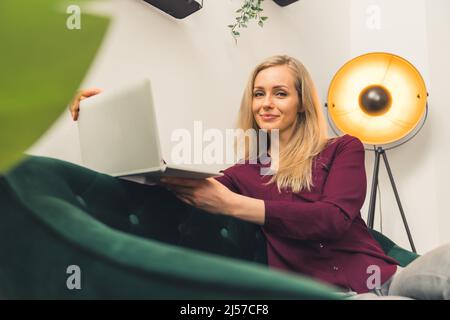 Hübsche kaukasische Frau sitzt auf dem Sofa mit einem Laptop nach Hause Hintergrund Remote Job Konzept kopieren Raum. Hochwertige Fotos Stockfoto