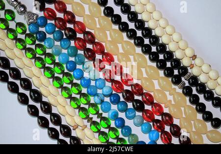 Bunte Gebetsperlen auf einem weißen Tisch. Gebetsperlen aus verschiedenen Materialien wie Holz, Metall, Glas, Knochen. Stockfoto