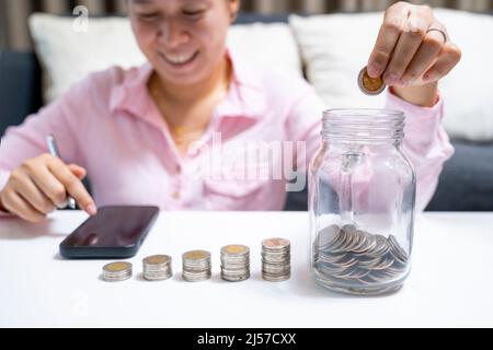 Weiblich rechnen über Geld sparen und legen Münze in Glas auf den Schreibtisch zu Hause. Stockfoto