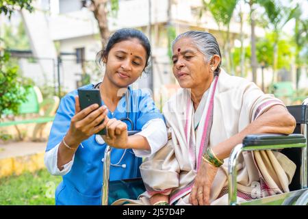 Krankenschwester zeigt Gesundheitstipps auf dem Handy, um den Patienten im Rollstuhl im Garten zu seniornen - Konzept der Technologie, Unterstützung und Betreuer. Stockfoto