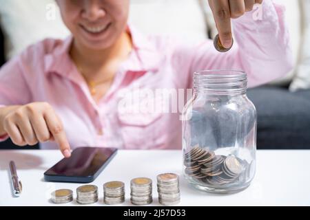 Weiblich rechnen über Geld sparen und legen Münze in Glas auf den Schreibtisch zu Hause. Stockfoto